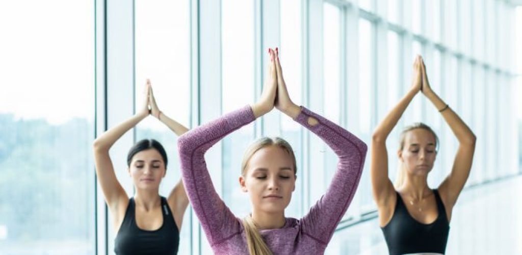 Rear view of three women meditate at yoga classes.
