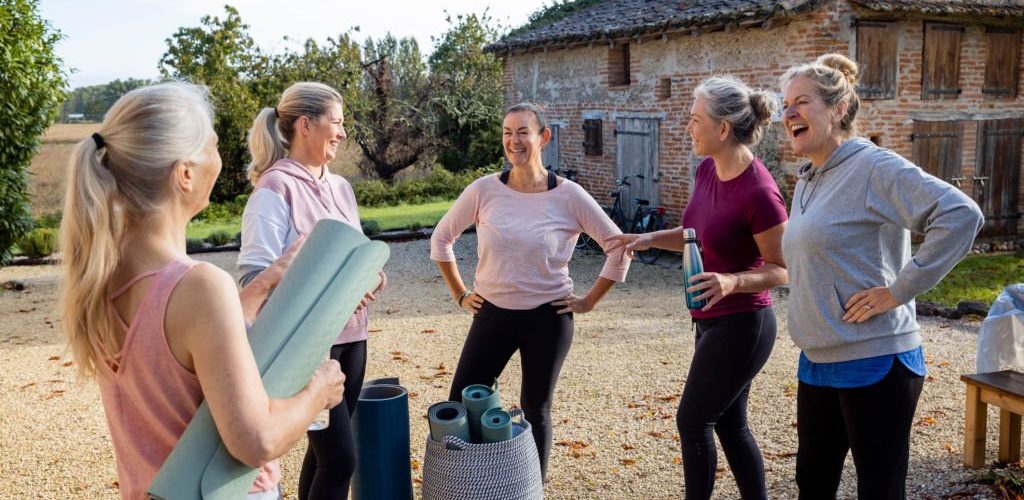 Group of mature women doing Yoga outdoors in France together while on a wellness vacation. They are all standing holding their mats ready to get started.