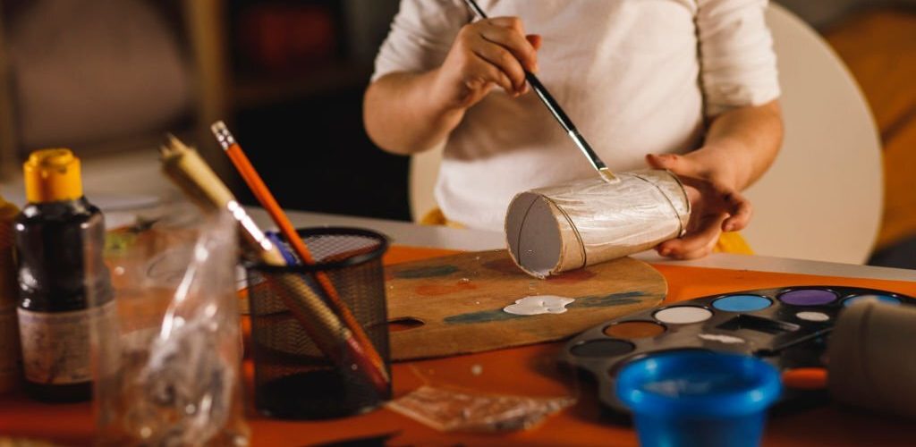 Midsection of unrecognizable little girl painting an empty roll of toilet paper while doing arts and crafts.
