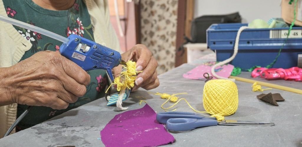Portrait of an artisan woman at home in her atelier, handcrafting a cloth doll with sustainable materials and cloth remains. Around her there are some tools such as a pen, scissors and sewing threads, used for manufacturing the cloth doll.