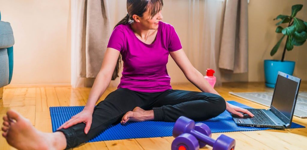 Young cheerful woman working out from home, online workout on laptop