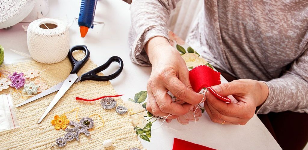 Senior women sews by hand and making heart shape ornament.